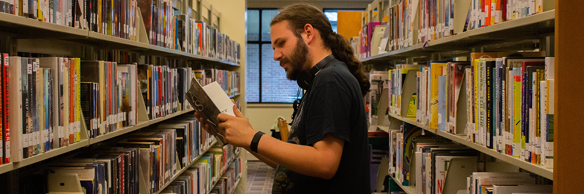 Man reading book in library book stacks