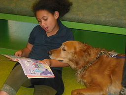 Child reading a book to a certified therapy dog