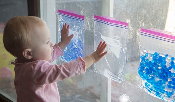 toddler playing with sensory bags taped to a window