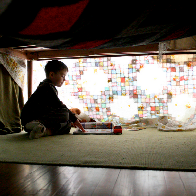 Child reading in a constructed blanket fort