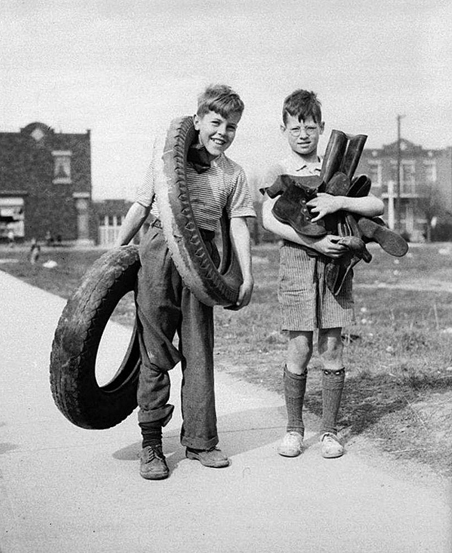 black and white photo of children carrying tires and rubber boots