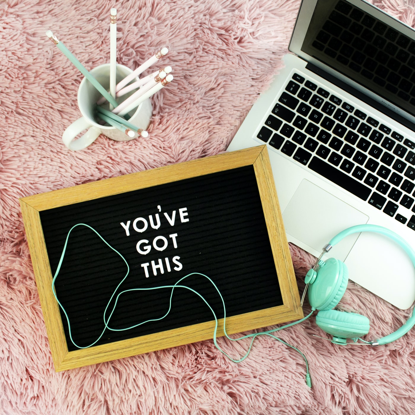 Computer, mug with pencils, headphones, and sign that says "you've got this"