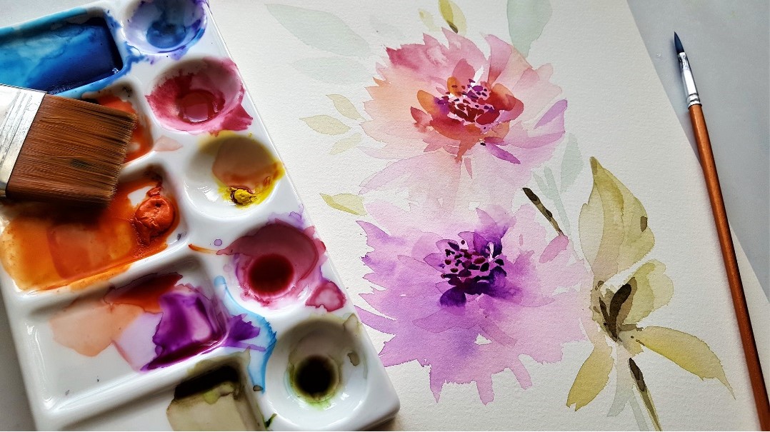 Image of watercolor paints in a tray on top of a canvas painted with watercolor flowers