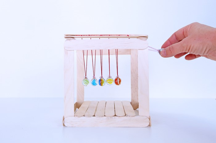white background with newton's cradle and a human hand in the foreground