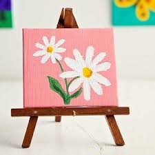 miniature easel with a miniature canvas painted pink with two white daisies painted on top