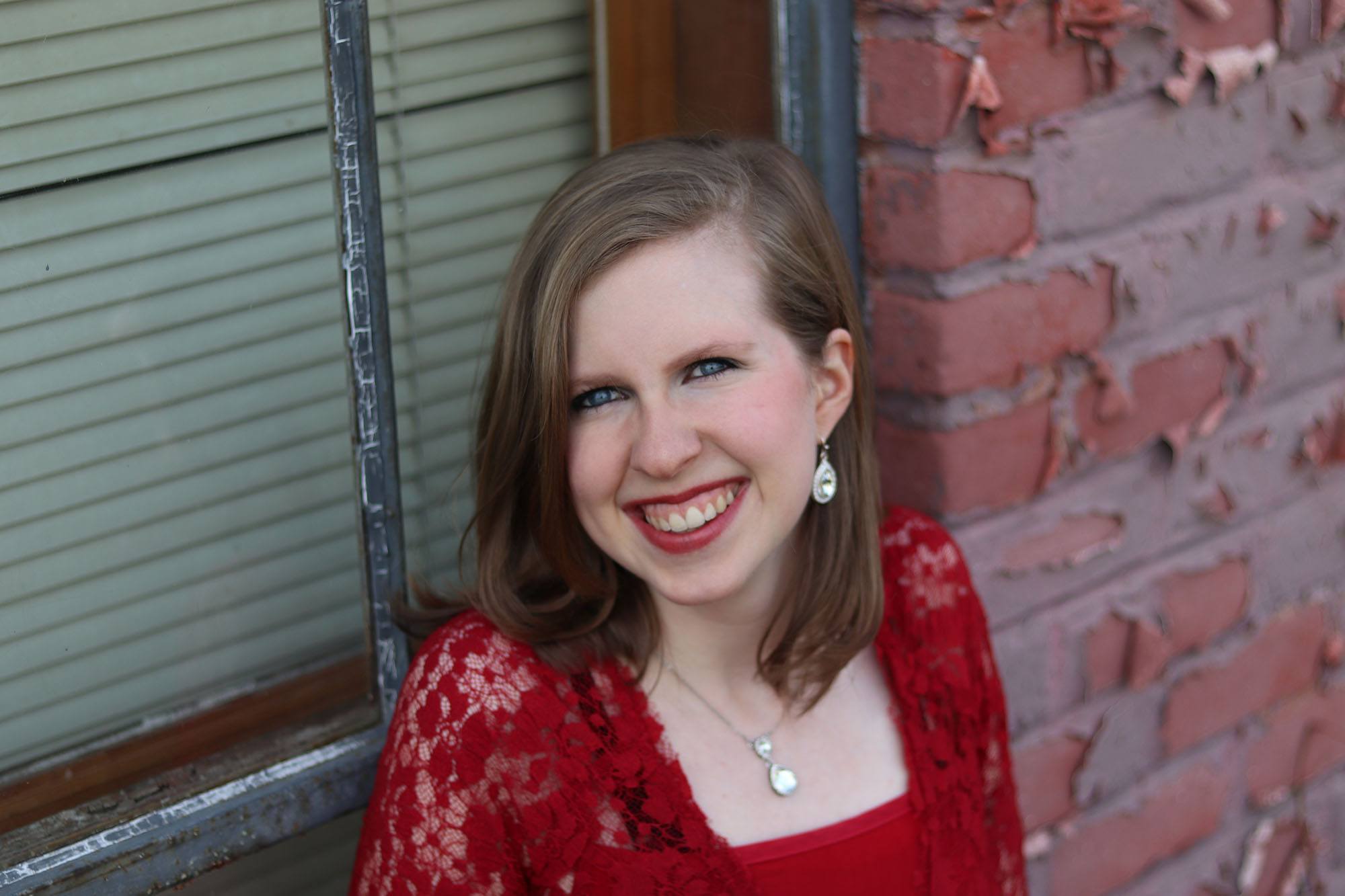 author Amanda Barratt wearing a red dress against a brick wall backdrop