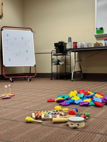 Photo of room with colorful toys on floor and coffee cart in background.